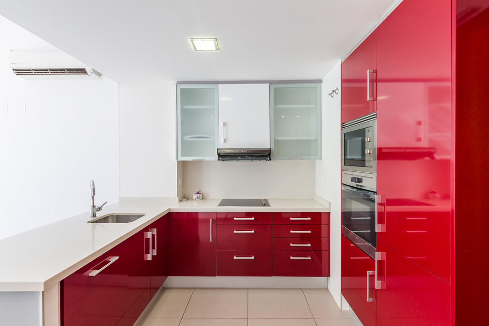 Пример оригинального дизайна: п-образная кухня в современном стиле с плоскими фасадами, красными фасадами, техникой из нержавеющей стали, врезной мойкой, белым фартуком, белым полом и белой столешницей