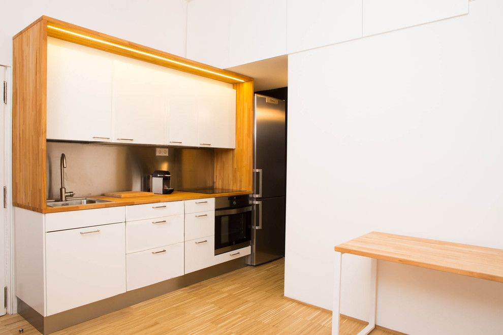 Inspiration för små skandinaviska linjära kök och matrum, med en enkel diskho, släta luckor, vita skåp, träbänkskiva, stänkskydd med metallisk yta, stänkskydd i metallkakel, rostfria vitvaror och mellanmörkt trägolv