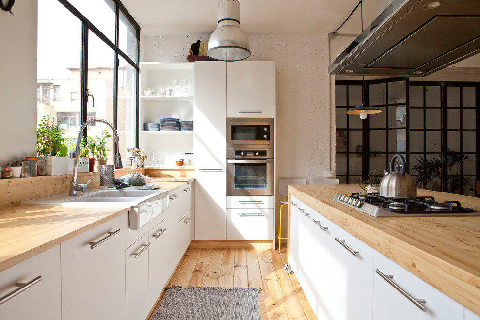 На фото: огромная прямая кухня-гостиная в скандинавском стиле с двойной мойкой, белыми фасадами, деревянной столешницей, техникой из нержавеющей стали, светлым паркетным полом и островом с