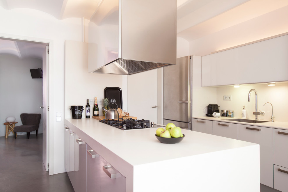 Design ideas for a medium sized modern galley open plan kitchen in Barcelona with a single-bowl sink, flat-panel cabinets, white cabinets, white splashback, stainless steel appliances, a breakfast bar and white worktops.