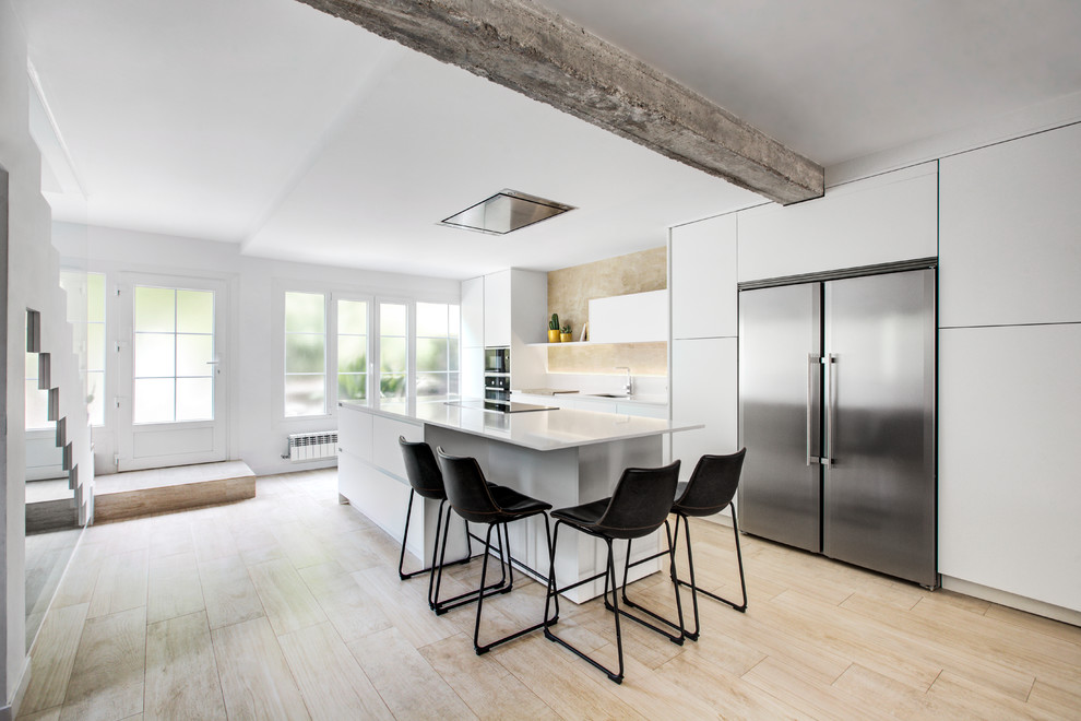 Design ideas for a scandinavian galley open plan kitchen in Madrid with flat-panel cabinets, white cabinets, stainless steel appliances, an island, white worktops, a submerged sink, beige splashback, light hardwood flooring and beige floors.