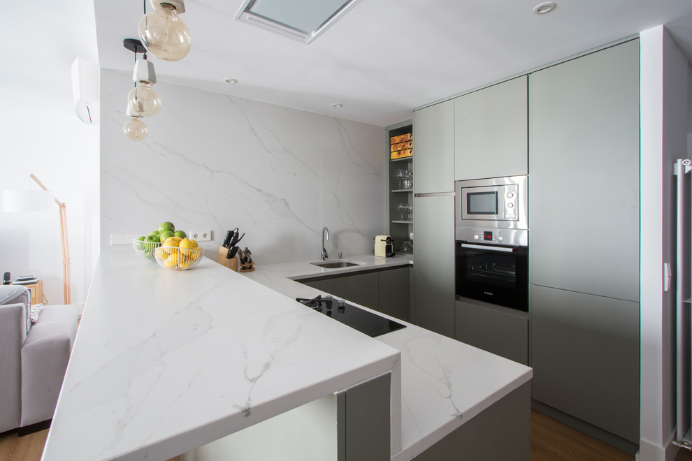 Foto på ett mellanstort funkis kök, med en undermonterad diskho, släta luckor, gröna skåp, marmorbänkskiva, vitt stänkskydd, stänkskydd i marmor, rostfria vitvaror, mellanmörkt trägolv, en halv köksö och brunt golv