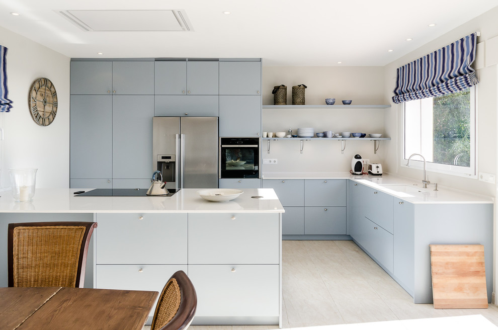 Cette image montre une cuisine ouverte nordique en L de taille moyenne avec un placard à porte plane, des portes de placard bleues, une crédence beige, un électroménager en acier inoxydable et une péninsule.