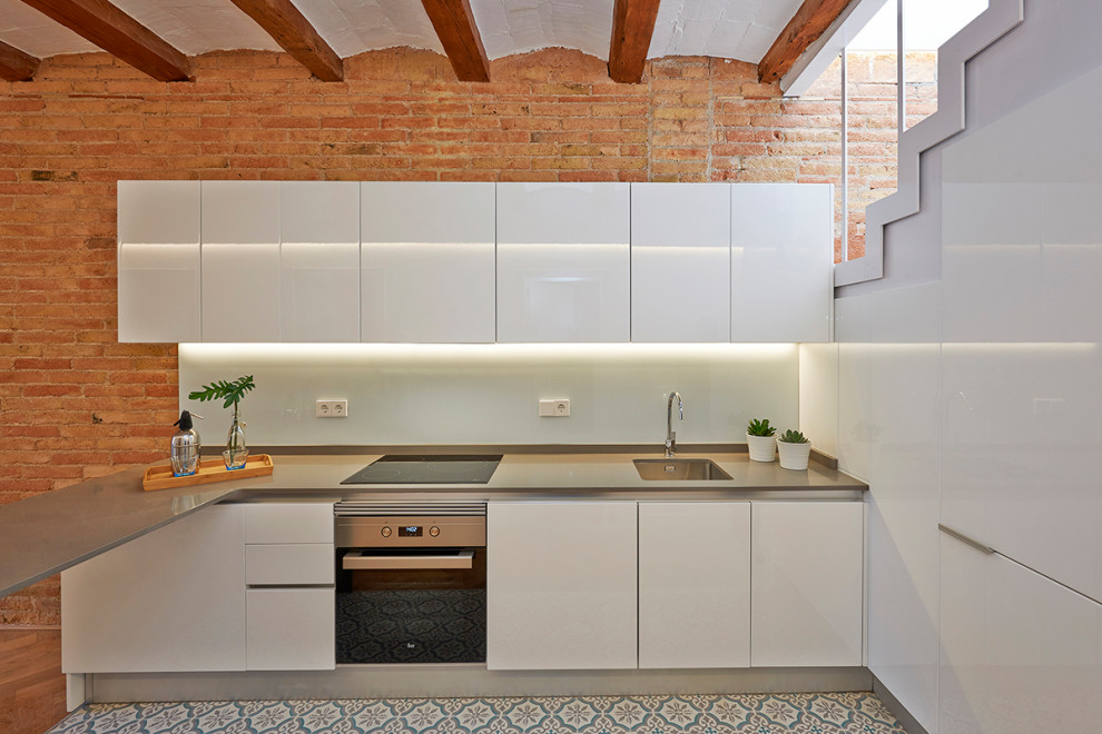 バルセロナにある地中海スタイルのおしゃれなペニンシュラキッチン (シングルシンク、フラットパネル扉のキャビネット、白いキャビネット、白いキッチンパネル、シルバーの調理設備、マルチカラーの床、グレーのキッチンカウンター、表し梁) の写真