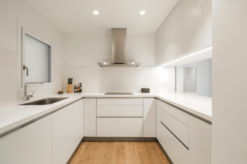 Mid-sized trendy u-shaped medium tone wood floor enclosed kitchen photo in Barcelona with an undermount sink, flat-panel cabinets, white cabinets, white backsplash, solid surface countertops, no island and white countertops