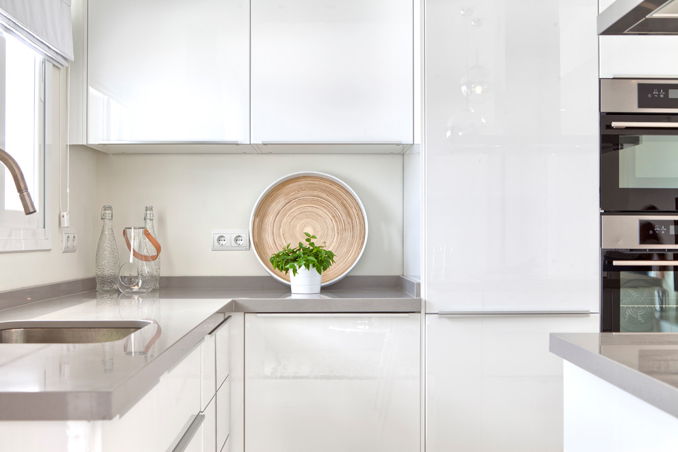 Example of a small danish l-shaped ceramic tile eat-in kitchen design in Malaga with a single-bowl sink, flat-panel cabinets, white cabinets, stainless steel appliances and an island