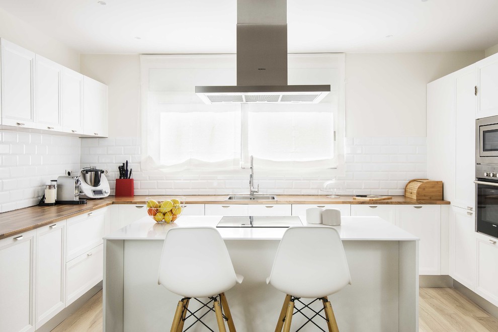 Example of a transitional u-shaped light wood floor and beige floor enclosed kitchen design in Barcelona with a single-bowl sink, wood countertops, white backsplash, subway tile backsplash, stainless steel appliances, an island, brown countertops, recessed-panel cabinets and white cabinets