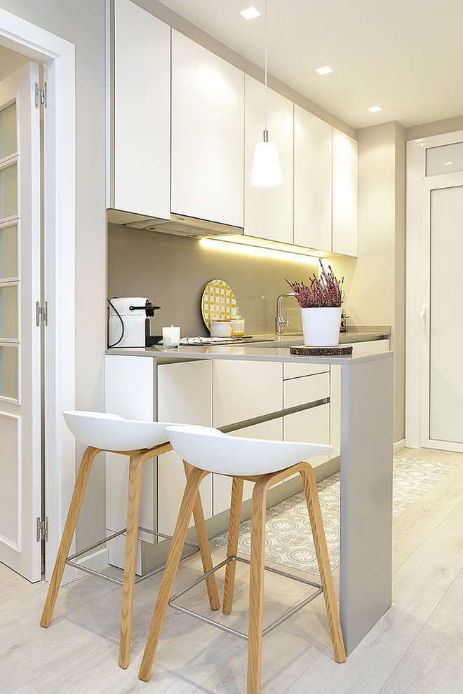 This is an example of a small scandi l-shaped enclosed kitchen in Barcelona with flat-panel cabinets, white cabinets, beige splashback, light hardwood flooring and a breakfast bar.