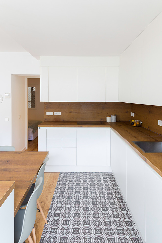 This is an example of a medium sized scandi l-shaped open plan kitchen in Barcelona with a single-bowl sink, flat-panel cabinets, white cabinets, wood worktops, brown splashback, wood splashback, integrated appliances, ceramic flooring, an island, grey floors and brown worktops.