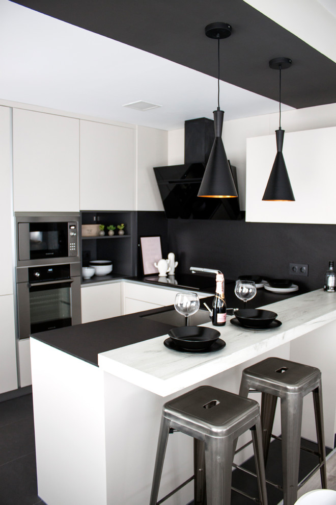 Immagine di una cucina ad U moderna di medie dimensioni con ante lisce, top in marmo, paraspruzzi nero, penisola, lavello sottopiano, elettrodomestici in acciaio inossidabile e pavimento nero