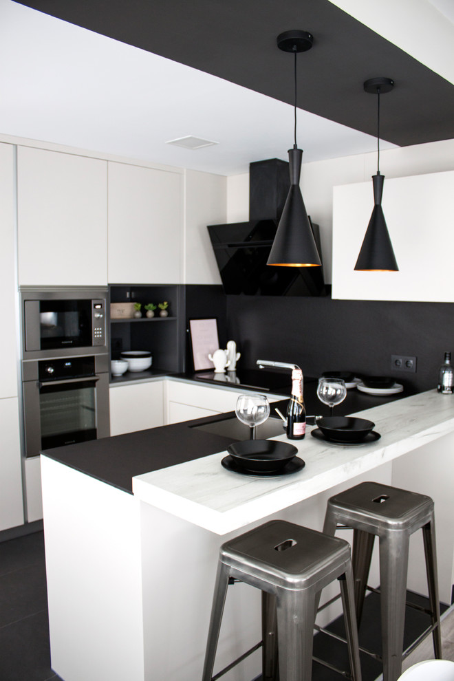 Kitchen - mid-sized modern u-shaped black floor kitchen idea in Madrid with flat-panel cabinets, white cabinets, marble countertops, black backsplash, a peninsula, an undermount sink and stainless steel appliances
