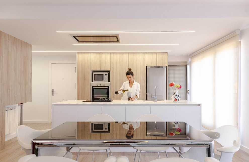 Пример оригинального дизайна: кухня в современном стиле с обеденным столом, врезной мойкой, плоскими фасадами, техникой из нержавеющей стали, светлым паркетным полом, островом и белой столешницей