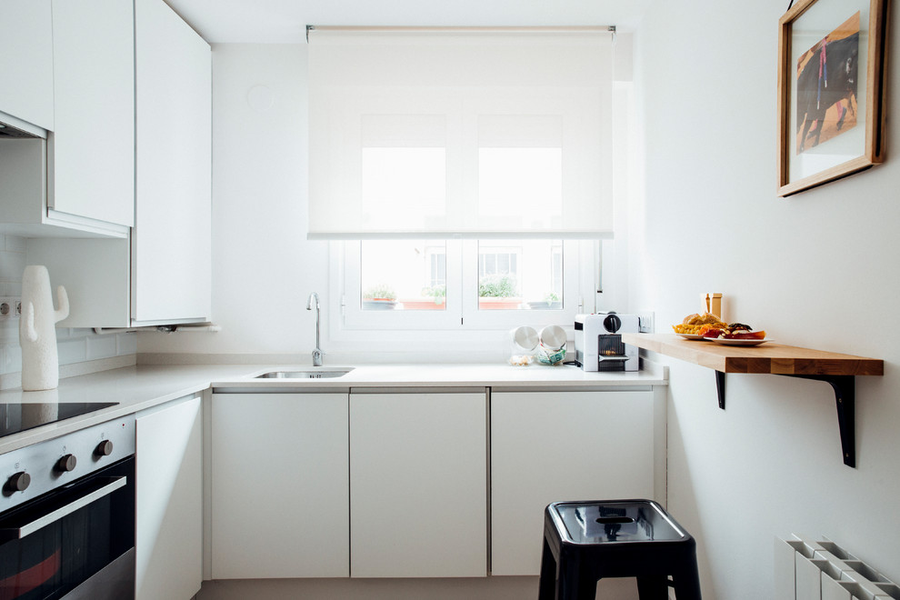 Bild på ett avskilt, litet minimalistiskt l-kök, med släta luckor, vita skåp och vitt stänkskydd