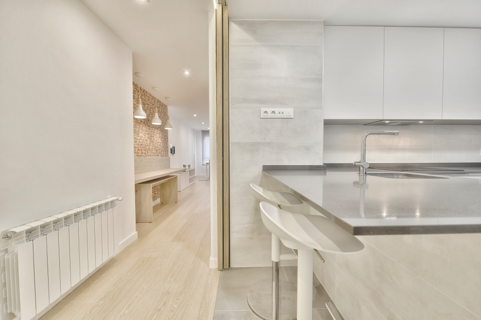 Bild på ett mellanstort minimalistiskt grå grått kök, med en undermonterad diskho, släta luckor, vita skåp, bänkskiva i kvarts, grått stänkskydd, stänkskydd i porslinskakel, rostfria vitvaror, klinkergolv i porslin, en halv köksö och grått golv
