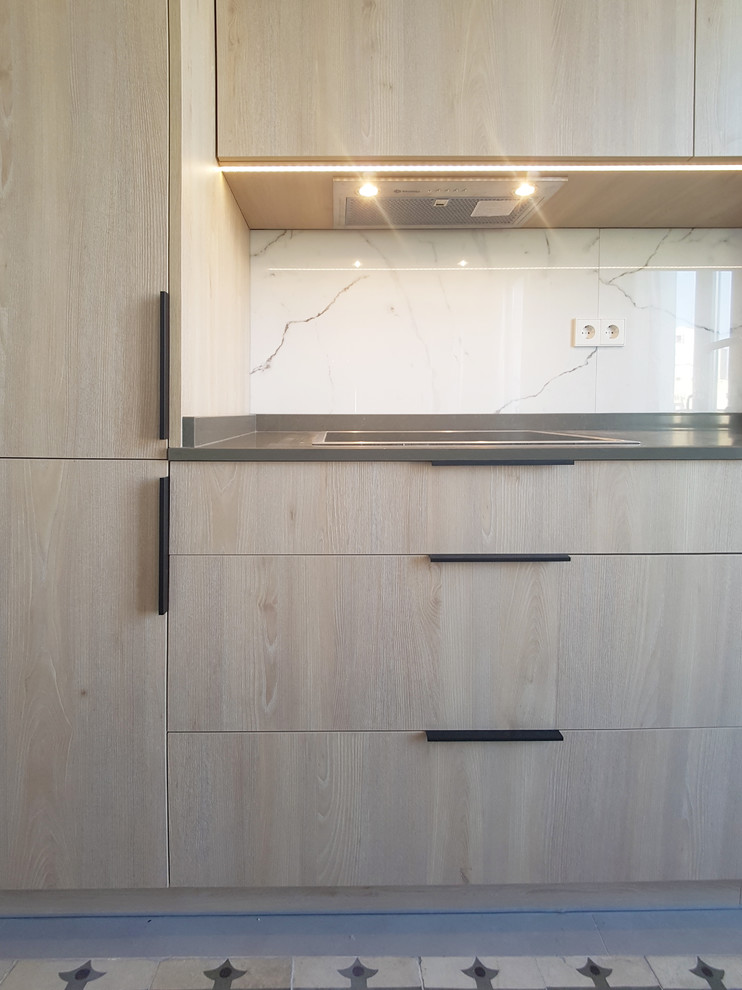 This is an example of a medium sized contemporary single-wall open plan kitchen in Madrid with a submerged sink, flat-panel cabinets, light wood cabinets, engineered stone countertops, white splashback, marble splashback, stainless steel appliances, cement flooring, an island and blue floors.
