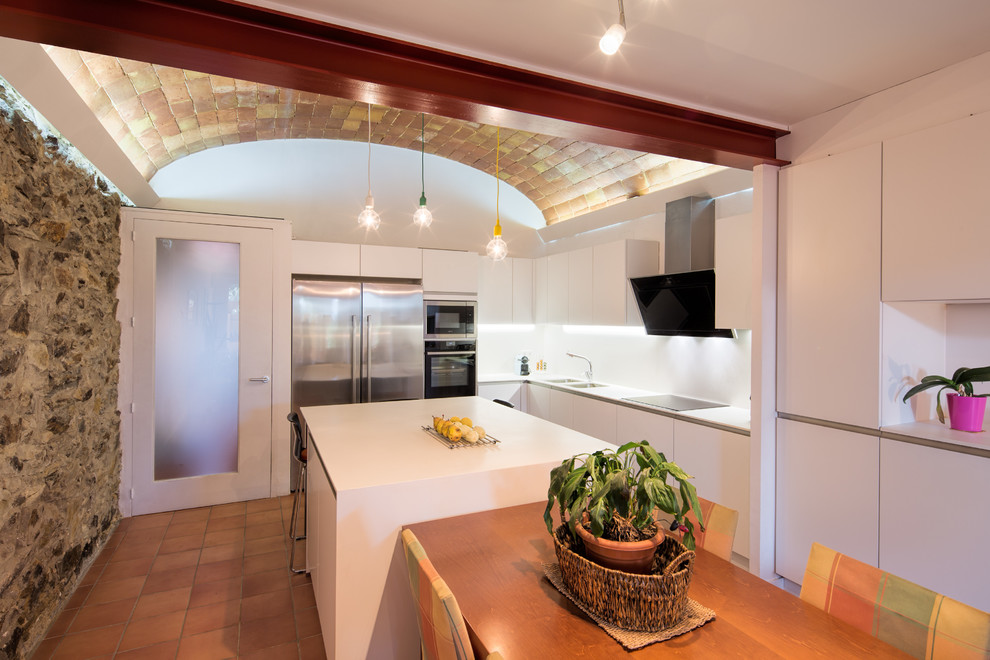 Modern inredning av ett mellanstort vit vitt kök med öppen planlösning, med en dubbel diskho, släta luckor, vita skåp, bänkskiva i kvarts, vitt stänkskydd, rostfria vitvaror, klinkergolv i terrakotta, en köksö och brunt golv