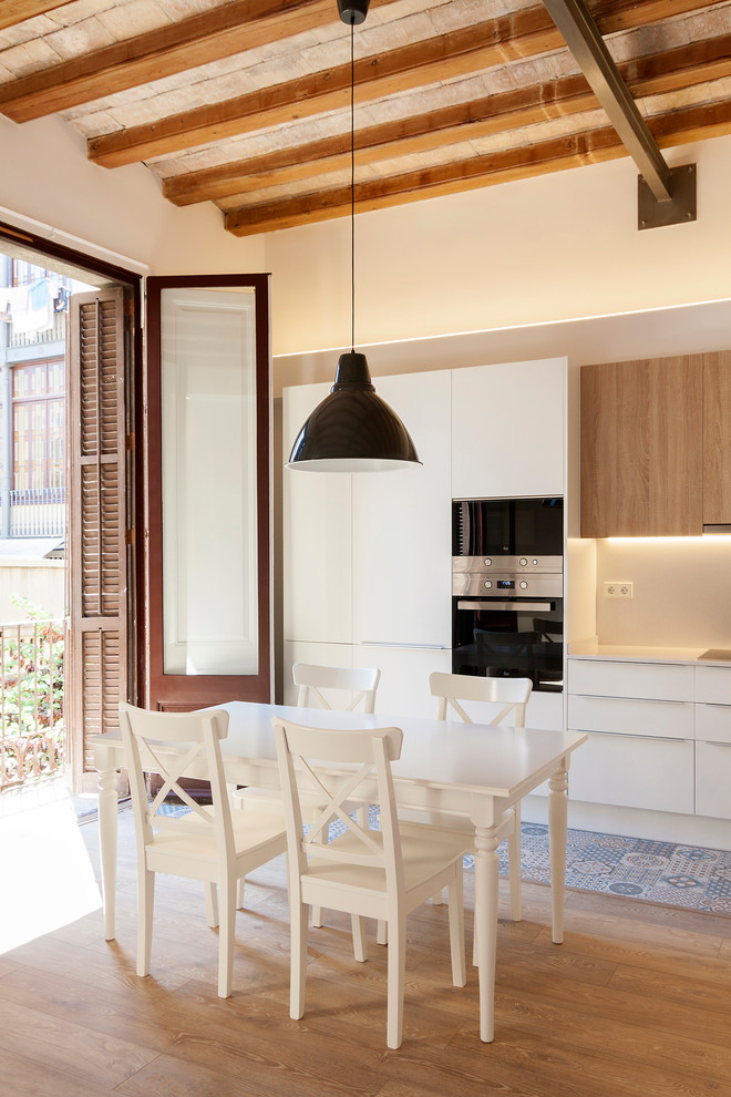 Example of a mid-sized tuscan single-wall medium tone wood floor eat-in kitchen design in Barcelona with flat-panel cabinets, white cabinets, white backsplash, stainless steel appliances and no island