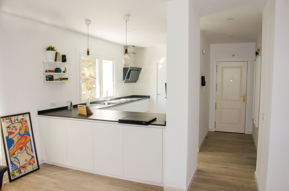 Immagine di una cucina minimal di medie dimensioni con lavello stile country, elettrodomestici neri, parquet chiaro, penisola, pavimento marrone e top nero