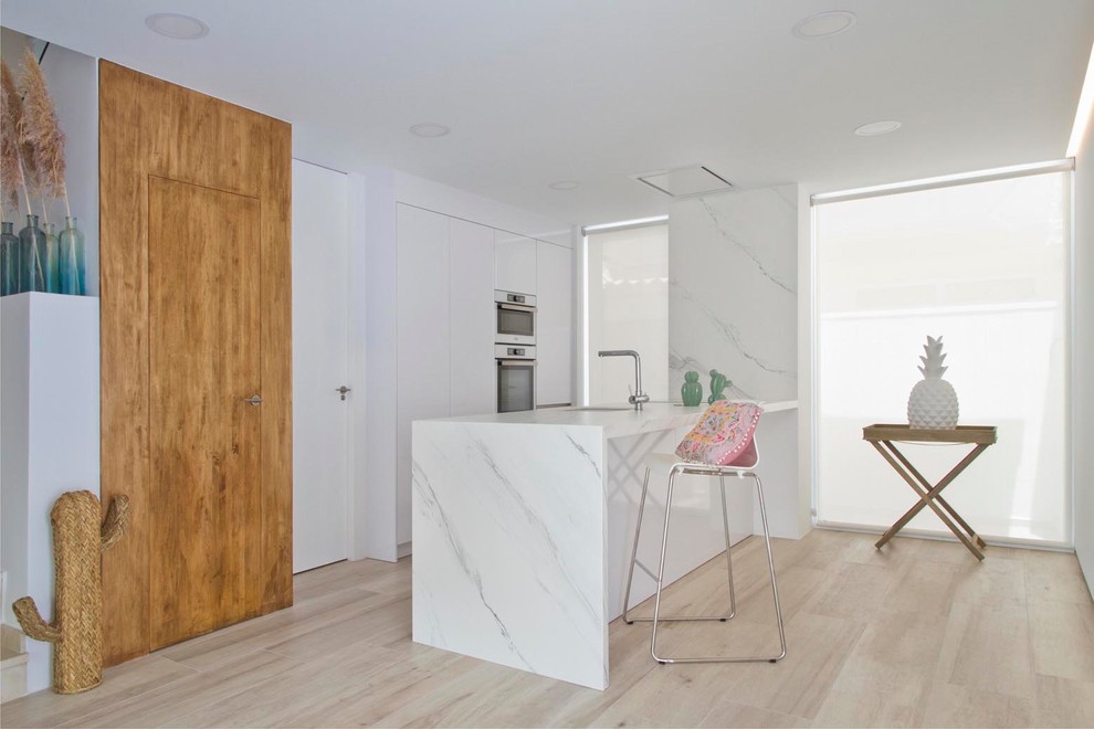 Contemporary l-shaped kitchen in Other with flat-panel cabinets, white cabinets, light hardwood flooring, a breakfast bar, beige floors and white worktops.