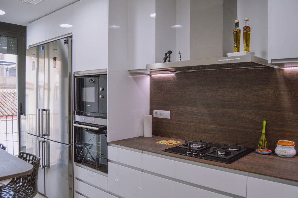 Photo of a medium sized shabby-chic style l-shaped enclosed kitchen in Barcelona with a submerged sink, flat-panel cabinets, white cabinets, laminate countertops, brown splashback, wood splashback, stainless steel appliances, ceramic flooring, brown floors and brown worktops.