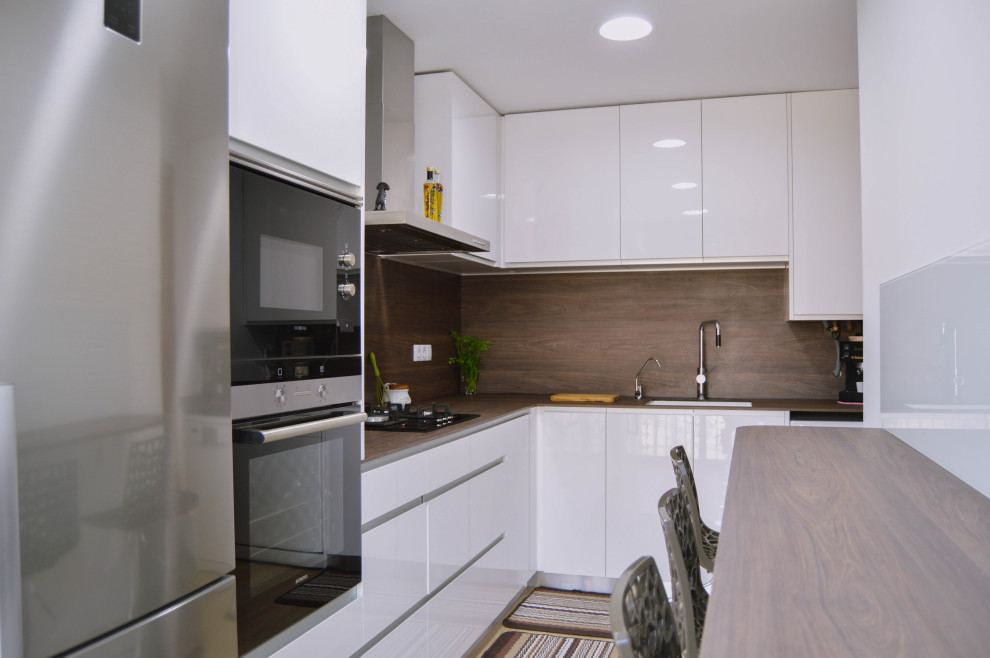 Medium sized vintage l-shaped enclosed kitchen in Barcelona with a submerged sink, flat-panel cabinets, white cabinets, laminate countertops, brown splashback, wood splashback, stainless steel appliances, ceramic flooring, brown floors and brown worktops.