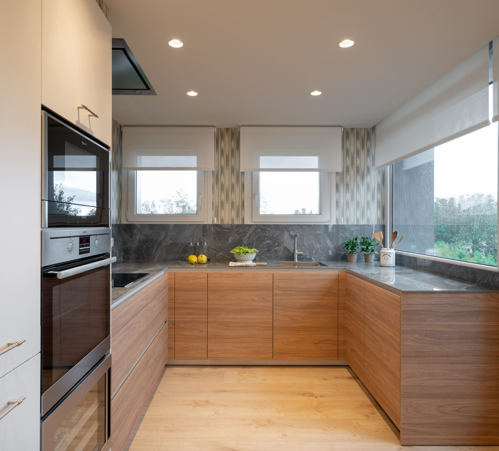 Foto på ett stort funkis grå kök, med en undermonterad diskho, släta luckor, vita skåp, bänkskiva i kvarts, grått stänkskydd, rostfria vitvaror, laminatgolv och brunt golv