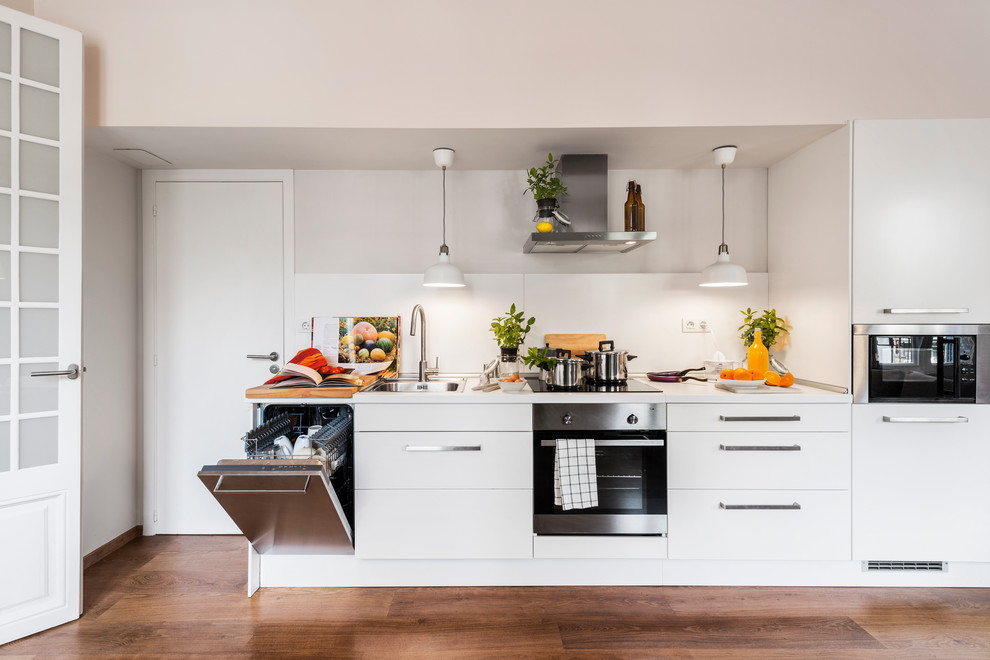 Diseño de cocina lineal escandinava con armarios con paneles lisos, puertas de armario blancas, salpicadero blanco y electrodomésticos de acero inoxidable