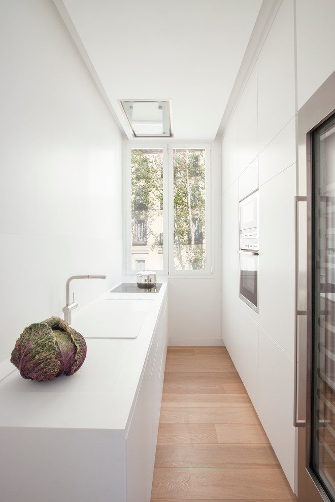 На фото: маленькая, узкая отдельная, параллельная кухня в стиле модернизм с монолитной мойкой, белыми фасадами, белым фартуком и светлым паркетным полом без острова для на участке и в саду с