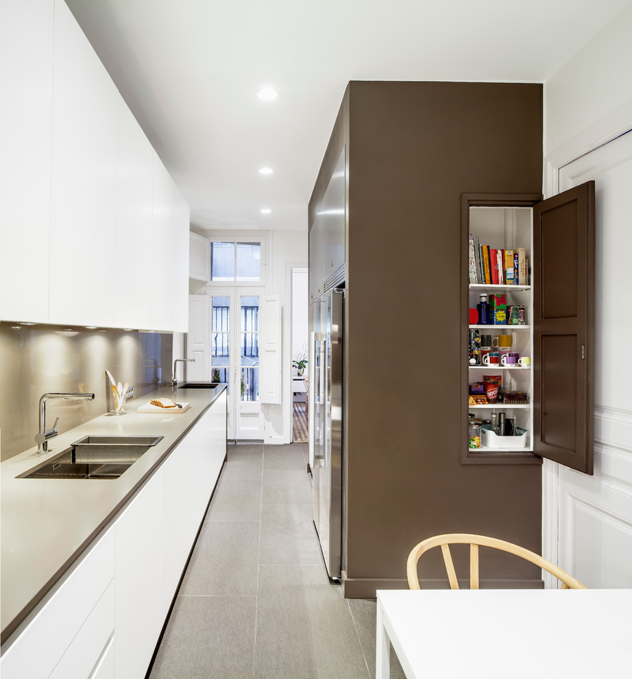 Einzeilige, Mittelgroße Moderne Wohnküche ohne Insel mit Waschbecken, flächenbündigen Schrankfronten, weißen Schränken, Küchengeräten aus Edelstahl und Keramikboden in Barcelona