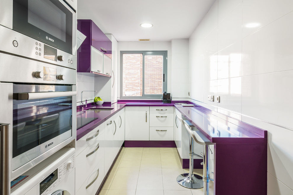 Moderne Küche in U-Form mit Unterbauwaschbecken, flächenbündigen Schrankfronten, weißen Schränken, Küchenrückwand in Weiß, Küchengeräten aus Edelstahl, beigem Boden und lila Arbeitsplatte in Sevilla