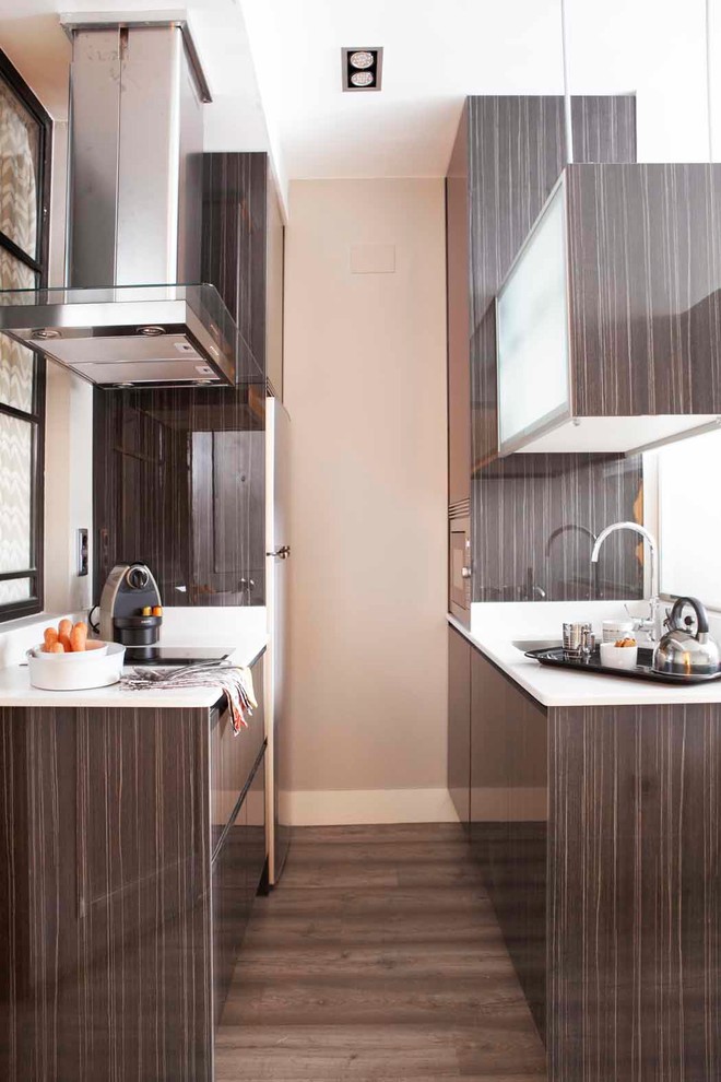 Foto de cocina estrecha contemporánea pequeña con armarios con paneles lisos, puertas de armario marrones, suelo de madera oscura y encimeras blancas