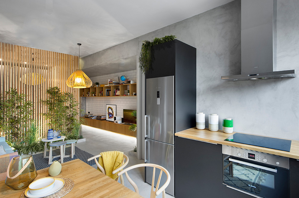 На фото: кухня-гостиная в стиле лофт с плоскими фасадами, черными фасадами, деревянной столешницей, серым фартуком, бетонным полом и серым полом