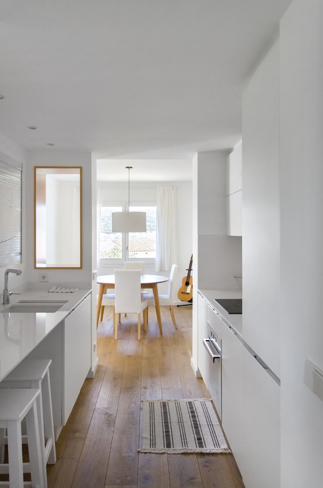 Cette photo montre une cuisine ouverte parallèle scandinave de taille moyenne avec un placard à porte plane, des portes de placard blanches, un sol en bois brun et aucun îlot.