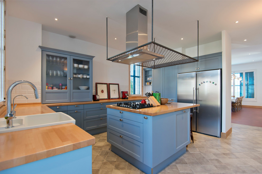 Inspiration for a rural galley enclosed kitchen in Barcelona with an integrated sink, shaker cabinets, blue cabinets, wood worktops, white splashback, metro tiled splashback, stainless steel appliances, an island and beige floors.