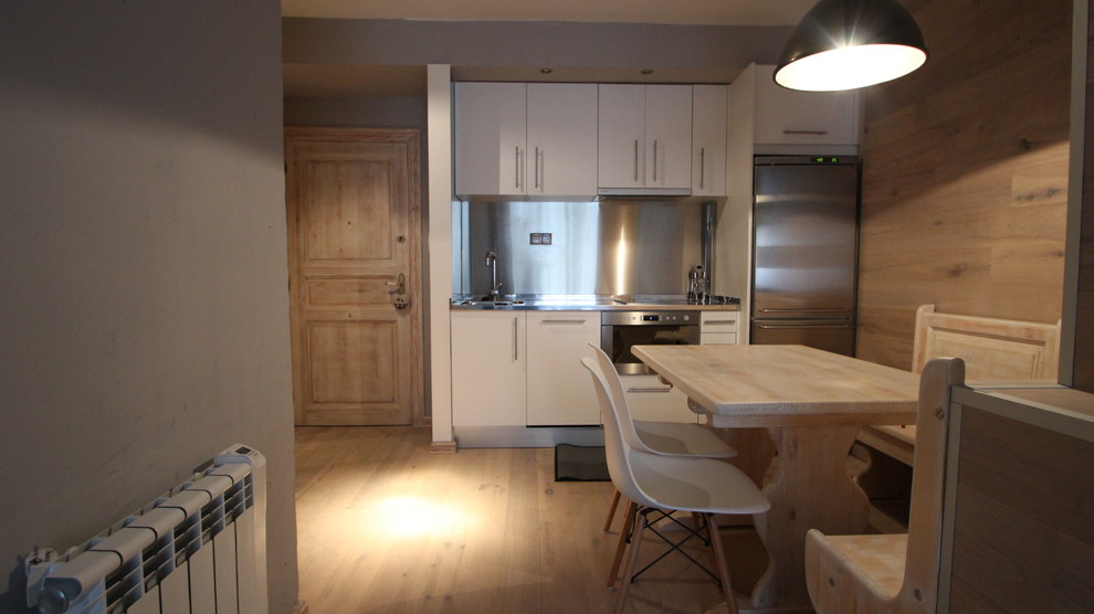 Cette image montre une petite cuisine ouverte linéaire nordique avec un évier intégré, des portes de placard blanches, un plan de travail en inox, un électroménager en acier inoxydable et parquet clair.