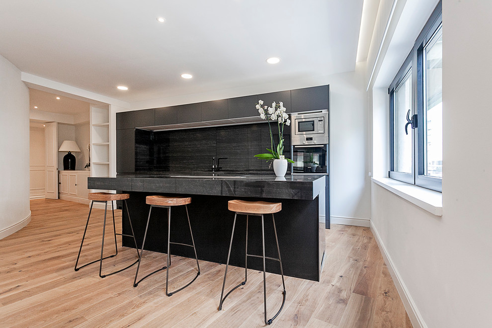 This is an example of a medium sized contemporary single-wall kitchen in Other with flat-panel cabinets, black cabinets, black splashback, stainless steel appliances, medium hardwood flooring, an island and brown floors.