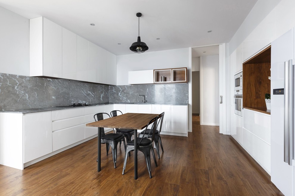 Bild på ett funkis kök och matrum, med släta luckor, vita skåp, grått stänkskydd, mörkt trägolv och vita vitvaror