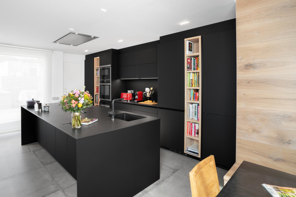 Aménagement d'une grande cuisine ouverte parallèle moderne avec un placard à porte plane, des portes de placard noires, une crédence noire, îlot, un sol gris et plan de travail noir.