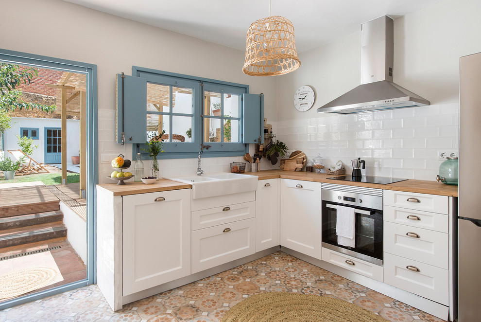 Small mediterranean l-shaped enclosed kitchen in Barcelona with a double-bowl sink, shaker cabinets, white cabinets, wood worktops, white splashback, ceramic splashback, stainless steel appliances, cement flooring, no island, multi-coloured floors and brown worktops.
