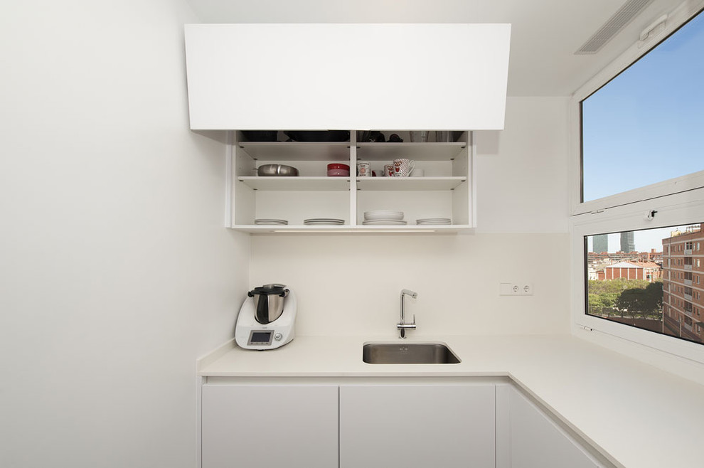 Modern inredning av ett avskilt, litet l-kök, med en enkel diskho, luckor med infälld panel, vita skåp, beige stänkskydd och svart golv