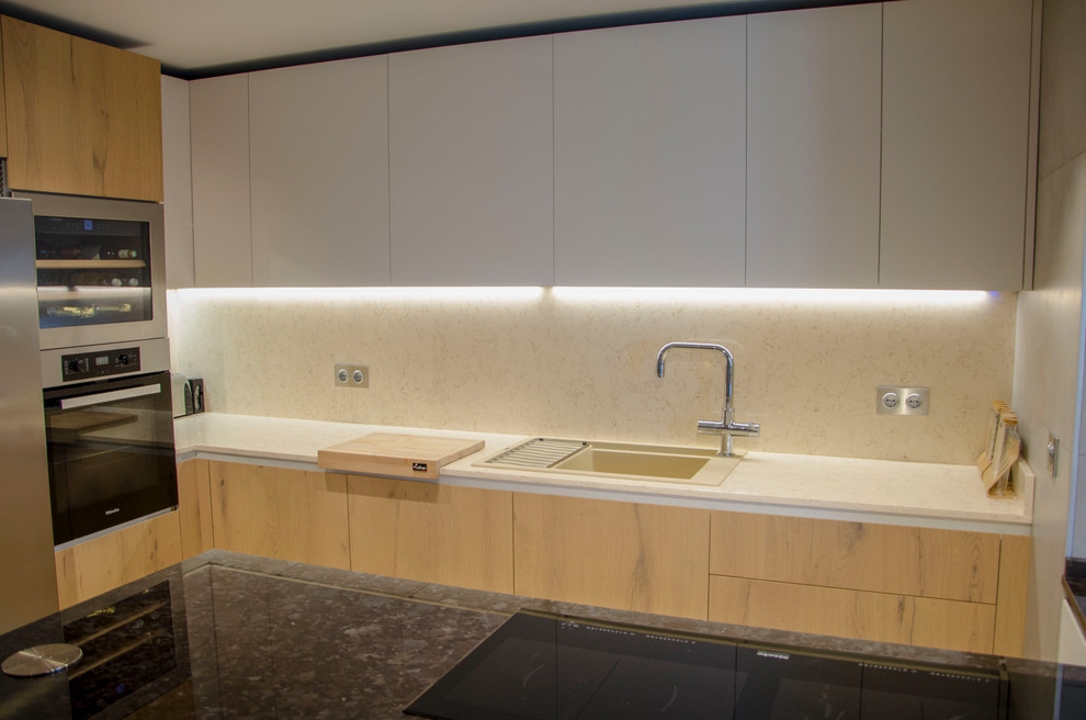 This is an example of a medium sized u-shaped kitchen/diner in Malaga with a belfast sink, glass-front cabinets, medium wood cabinets, granite worktops, stainless steel appliances, ceramic flooring, a breakfast bar, beige floors and black worktops.