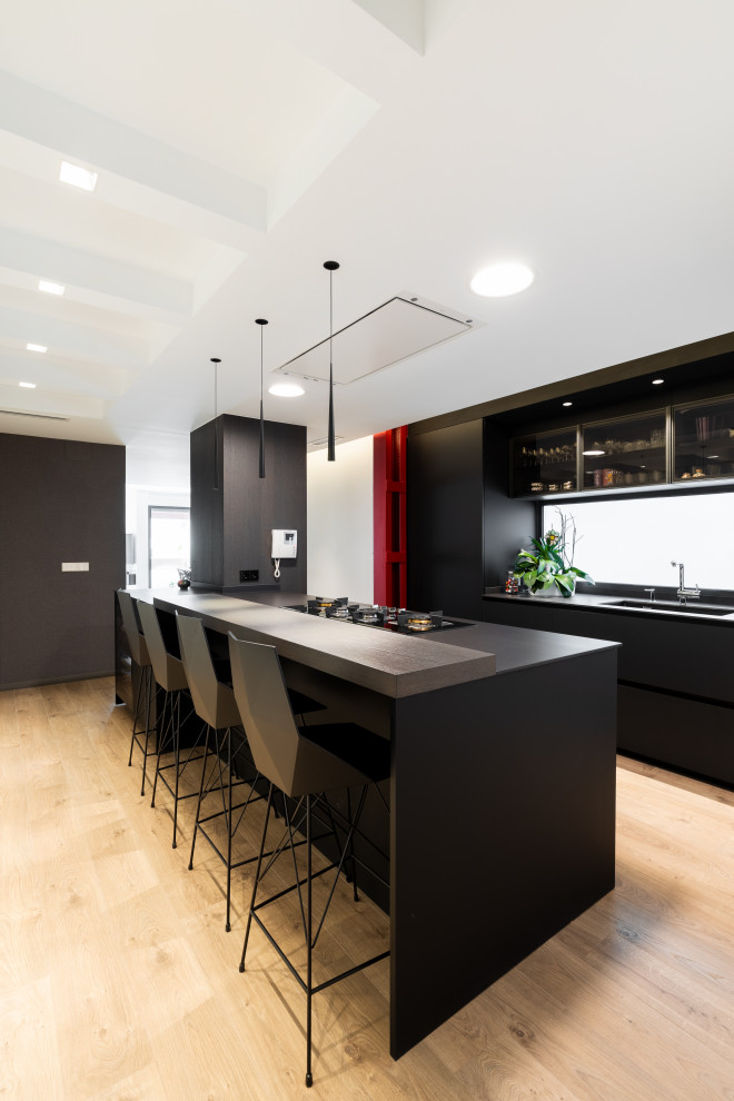 Immagine di una grande cucina contemporanea con elettrodomestici neri, pavimento in legno massello medio, top nero, ante lisce, ante nere, paraspruzzi a specchio e pavimento beige