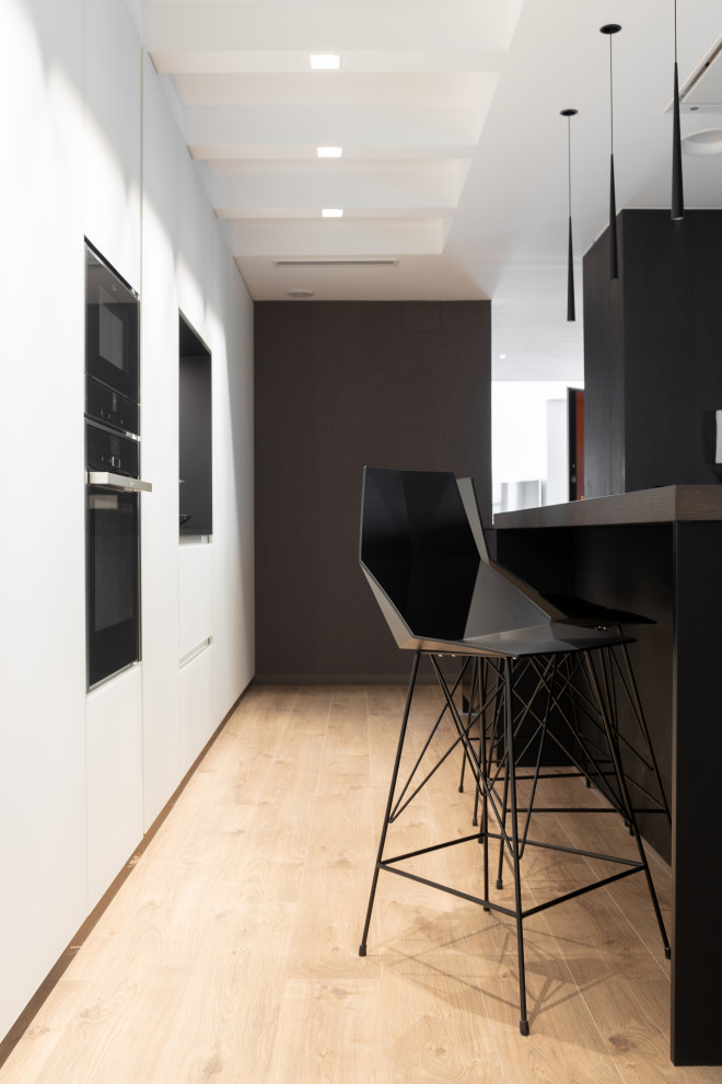 Offene, Große Moderne Küche mit schwarzen Elektrogeräten, braunem Holzboden, Kücheninsel und schwarzer Arbeitsplatte in Valencia