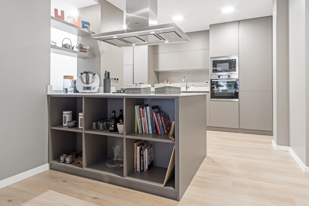 Large modern single-wall kitchen/diner in Madrid with a submerged sink, flat-panel cabinets, grey cabinets, engineered stone countertops, white splashback, stainless steel appliances, laminate floors and a breakfast bar.