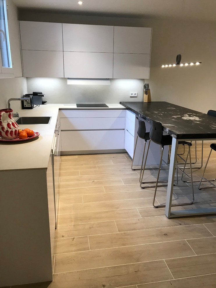 This is an example of a large modern u-shaped open plan kitchen in Madrid with a single-bowl sink, flat-panel cabinets, white cabinets, granite worktops, black splashback, stone slab splashback, stainless steel appliances, ceramic flooring, a breakfast bar and beige floors.