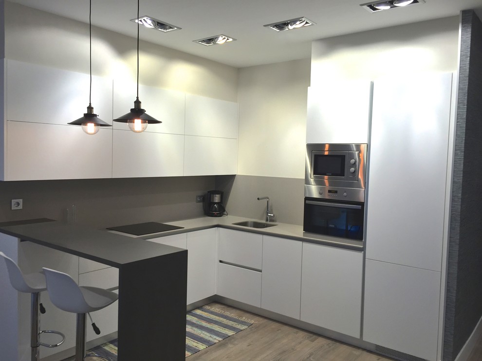 This is an example of a medium sized contemporary u-shaped open plan kitchen in Other with flat-panel cabinets, white cabinets, stainless steel appliances, medium hardwood flooring, a single-bowl sink and a breakfast bar.