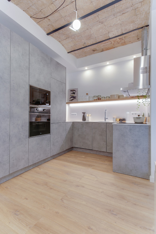Immagine di una cucina a L industriale con ante lisce, ante grigie, elettrodomestici neri, parquet chiaro, nessuna isola e pavimento beige