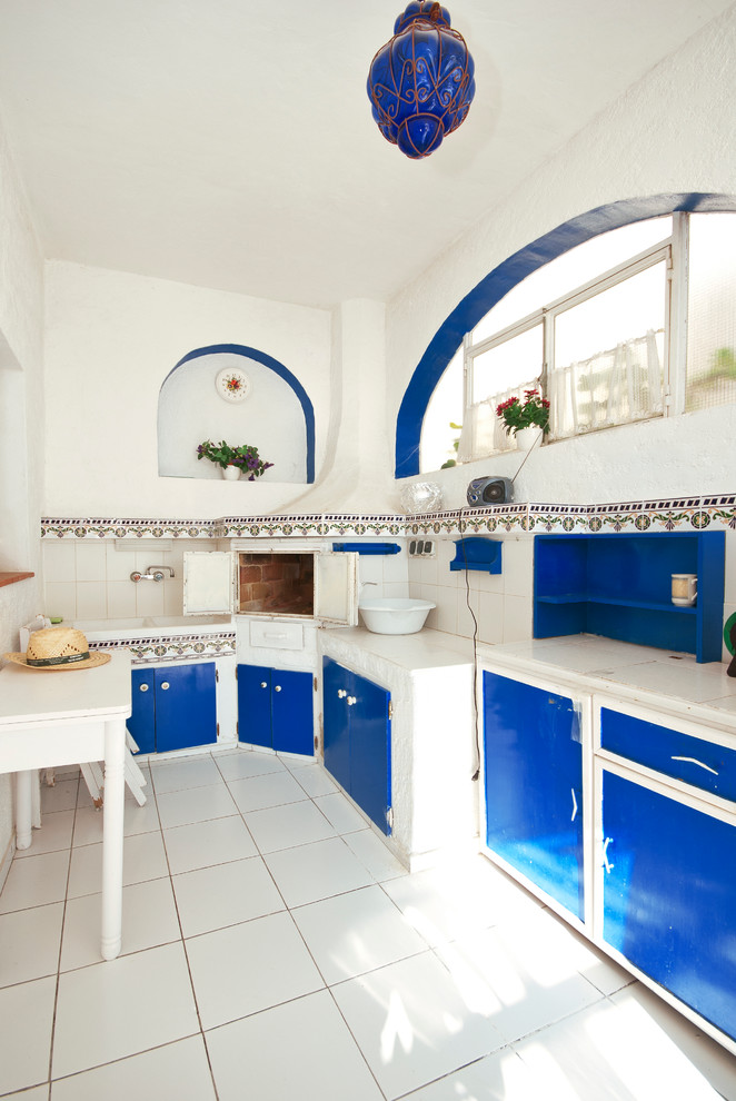 Immagine di una cucina a L mediterranea chiusa e di medie dimensioni con lavello a doppia vasca, ante blu, paraspruzzi bianco, ante lisce, pavimento con piastrelle in ceramica, nessuna isola e struttura in muratura