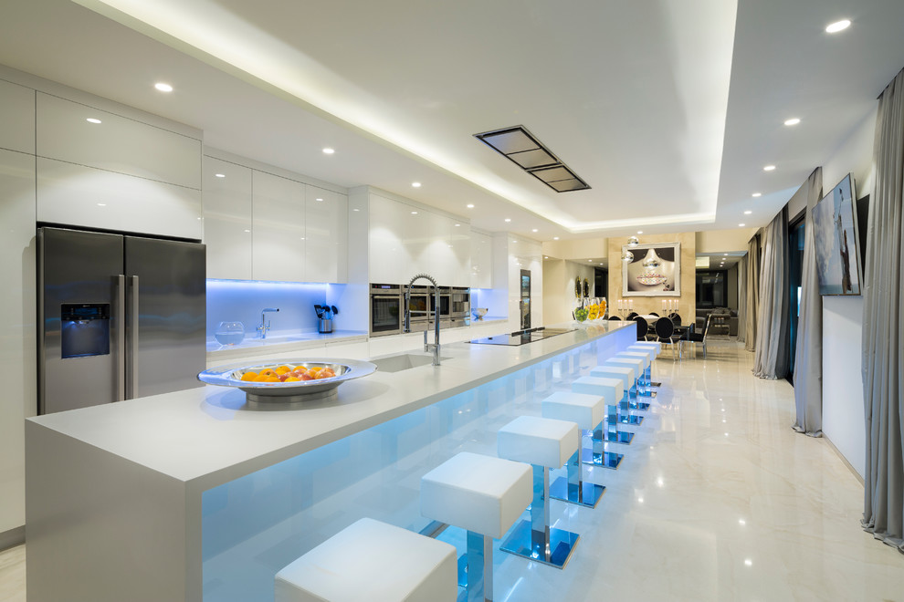 Foto på ett mycket stort funkis kök och matrum, med en undermonterad diskho, släta luckor, vita skåp, vitt stänkskydd, rostfria vitvaror och en köksö