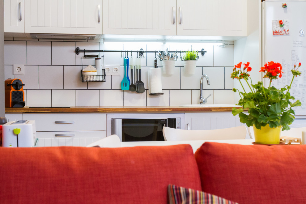 Foto på ett litet funkis linjärt kök med öppen planlösning, med en nedsänkt diskho, släta luckor, vita skåp, träbänkskiva, vitt stänkskydd, stänkskydd i keramik, vita vitvaror och mellanmörkt trägolv